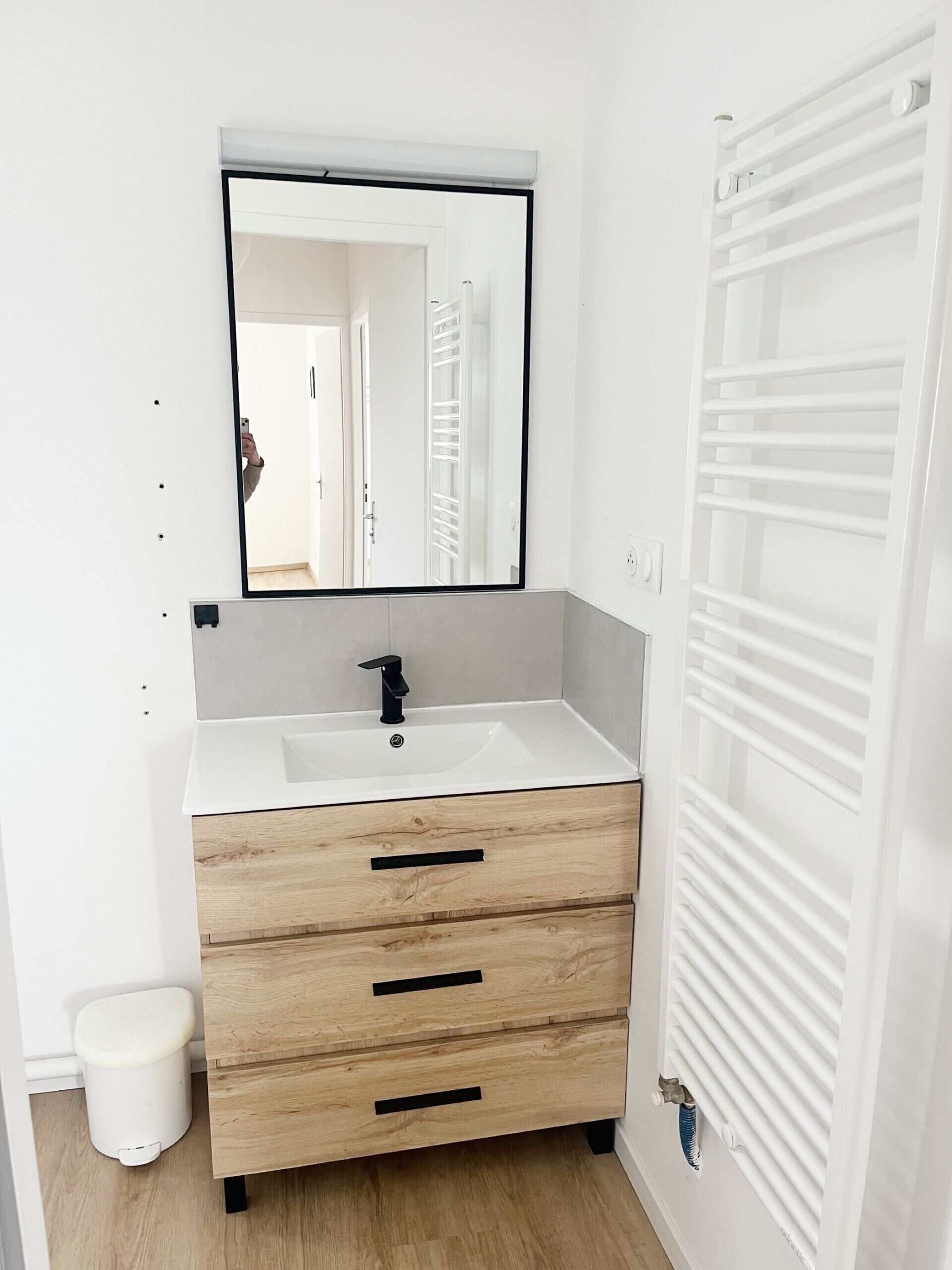 Een badkamer met een witte wastafel, een spiegel, een houten wastafelmeubel met lades, een wit toilet en een witte radiator.