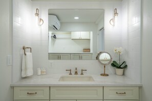 Un bagno con pareti piastrellate di bianco, un lavabo con dettagli dorati, uno specchio e un'orchidea in vaso.