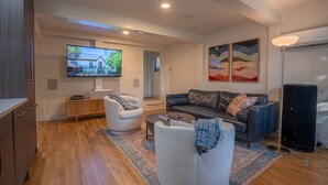 A modern living room with a flat-screen TV, a leather sofa, a white armchair, and a coffee table. - Travis Heights Gem! Walk to Lady Bird Lake & SoCo (Austin)