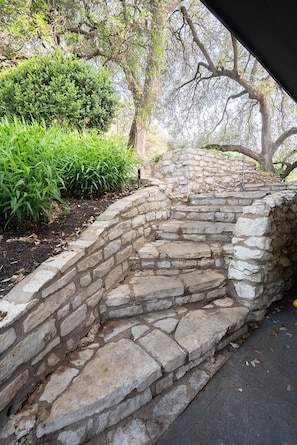 A stone staircase leading up to a stone wall, surrounded by greenery and trees. - Travis Heights Gem! Walk to Lady Bird Lake & SoCo (Austin)