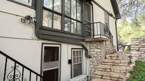A two-story house with a stone staircase, a balcony with a black railing, and a large window with blinds. - Travis Heights Gem! Walk to Lady Bird Lake & SoCo (Austin)