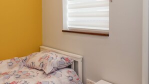 Ein Schlafzimmer mit Bett, einem Fenster mit Jalousien und einer gelben Wand.