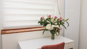 Ein weißer Schreibtisch mit Blumen in einer Vase, ein roter Sessel und ein Fenster mit Jalousien.