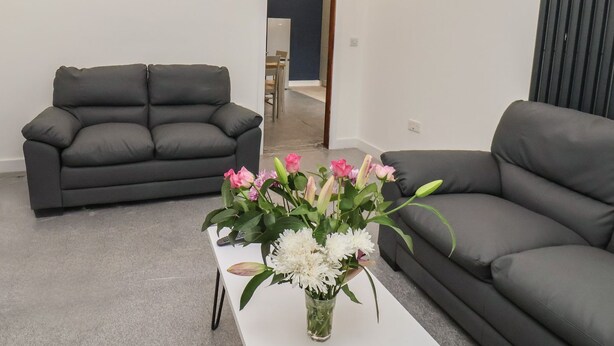 Ein Wohnzimmer mit zwei grauen Sofas, einem weißen Couchtisch mit Blumenarrangement und vier an der Wand befestigten Kunstwerken, die Meereslebewesen zeigen.