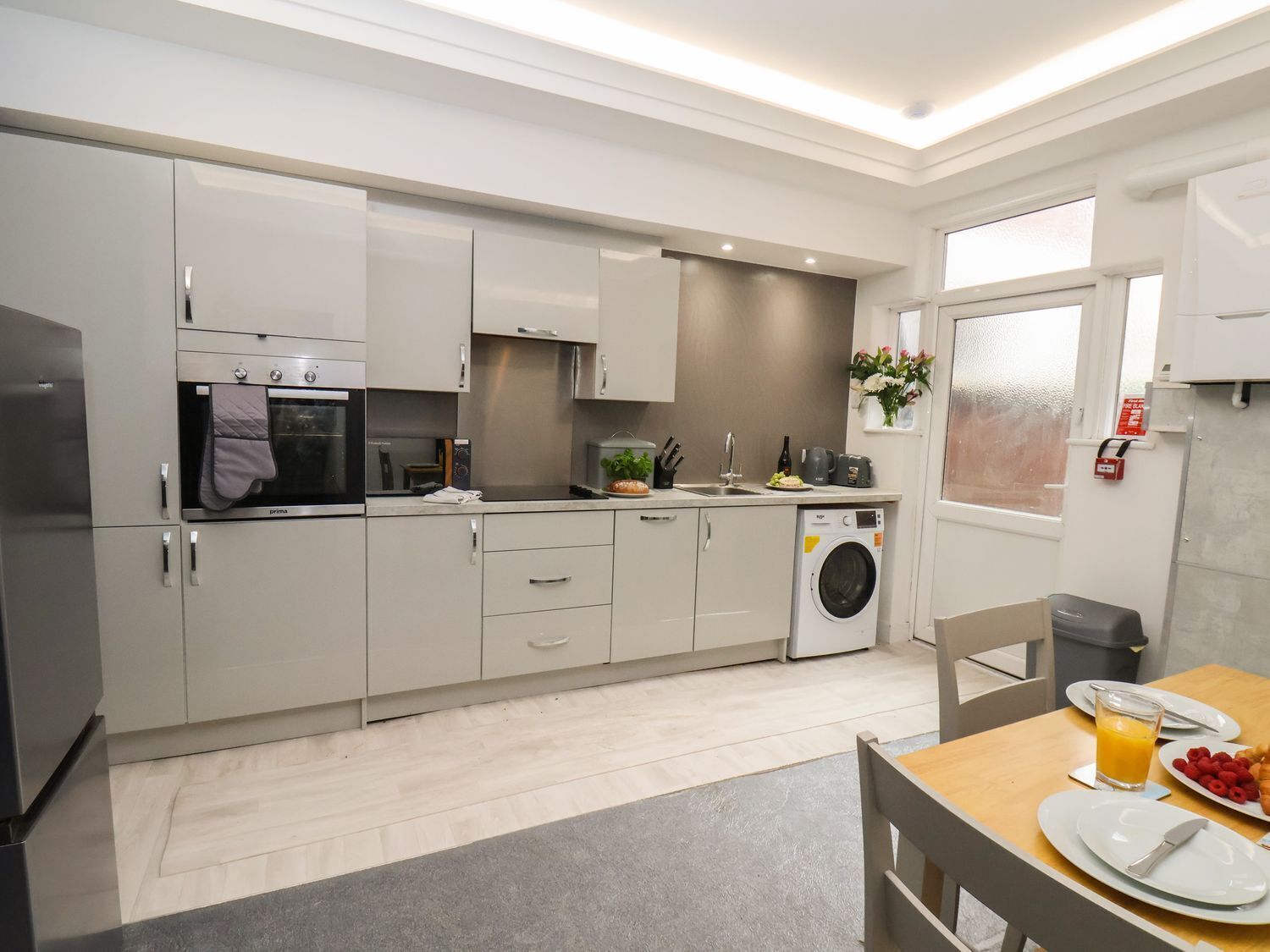 A modern kitchen with a washing machine, a dining table with breakfast, and a window with a view.