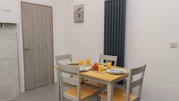 A dining area with a table set for two, a refrigerator, a door, and a radiator.