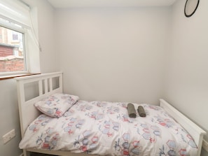 A small, white, single-bed room with a window, a white headboard, and a patterned bedspread. - Frankies Seaview 2 (Bridlington)