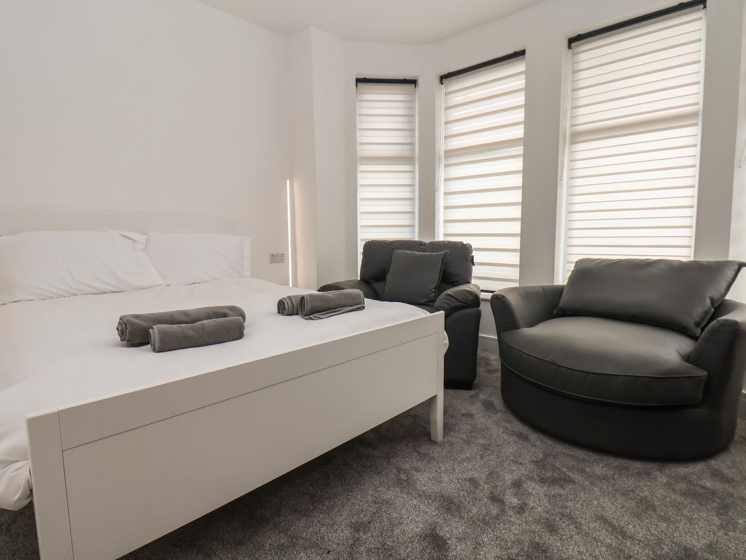 Une chambre d’hôtel moderne, équipée d’un lit, de deux fauteuils et de grandes fenêtres avec stores.