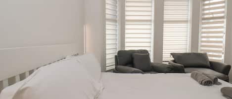 A bedroom with a bed, two armchairs, and a window with blinds.