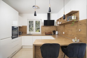 A modern kitchen with white cabinets, a wooden countertop, two black chairs, and pendant lights. - Villa Eman in Pula (Pula)