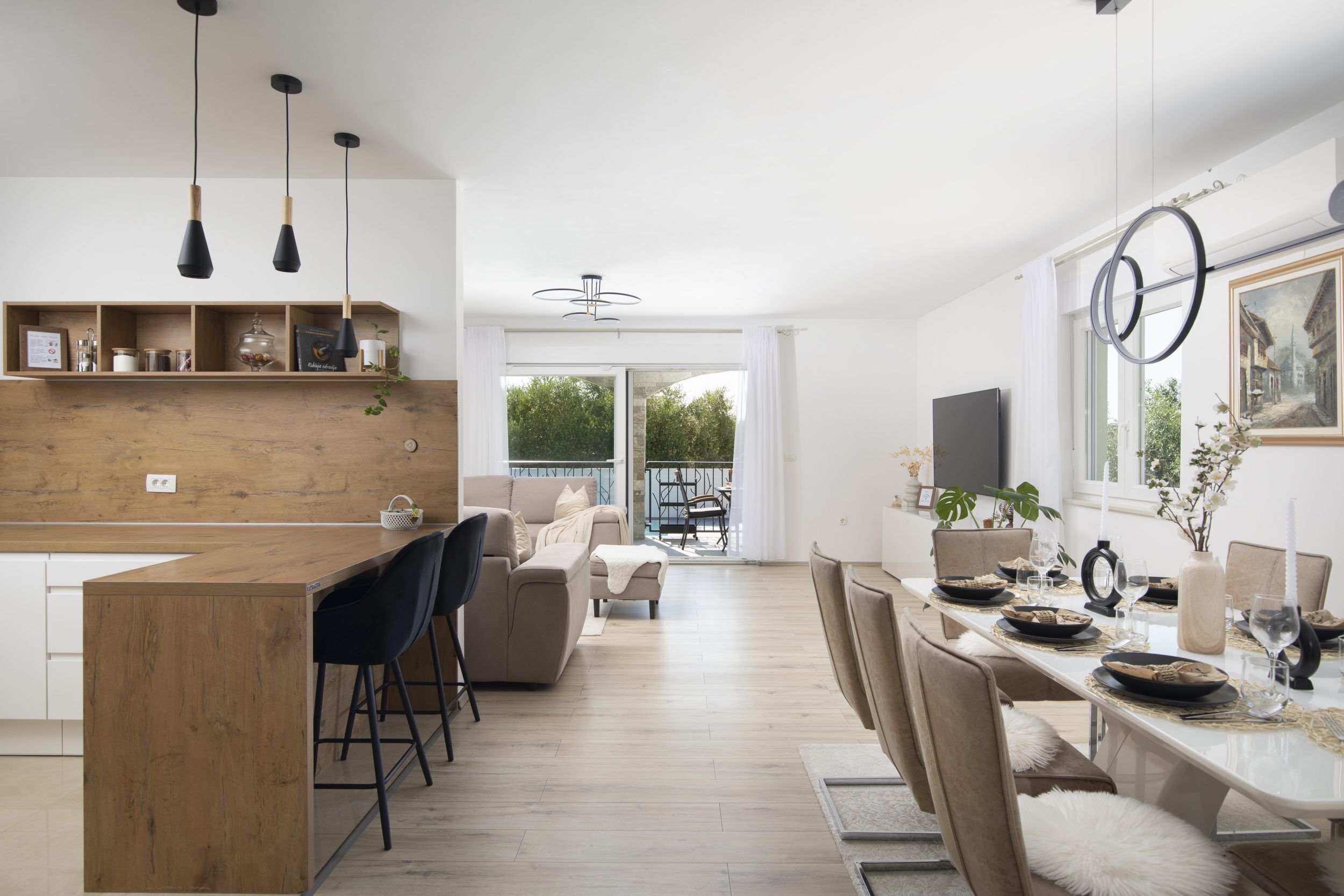 A modern kitchen with a wooden island, bar stools, and a dining area with a white table set for six.