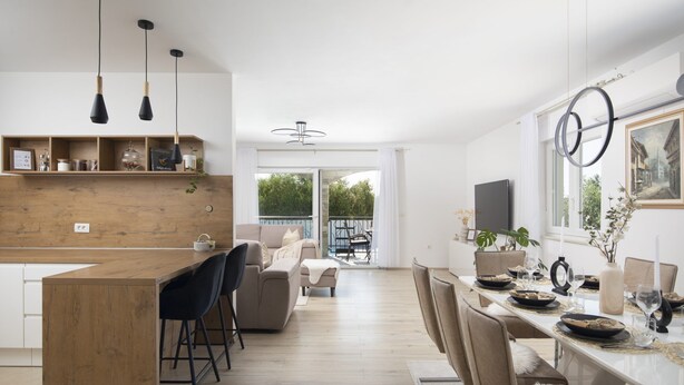 Eine moderne Küche mit einer Holz-Kochinsel, Barhocker und einem Essbereich mit einem weißen Tisch, gedeckt für sechs Personen.