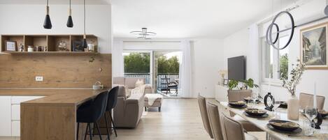 A modern kitchen with a wooden island, bar stools, and a dining area with a white table set for six.