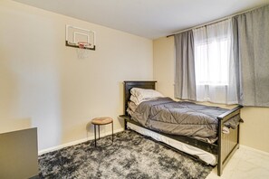 A bedroom with a bed, a small stool, a basketball hoop, and a window with curtains. - 2-bedroom house in Quiet Youngtown with cool AC & laundry room- (Youngtown)