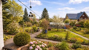 Un jardín residencial con un camino, plantas florecientes y una torre de campanas.