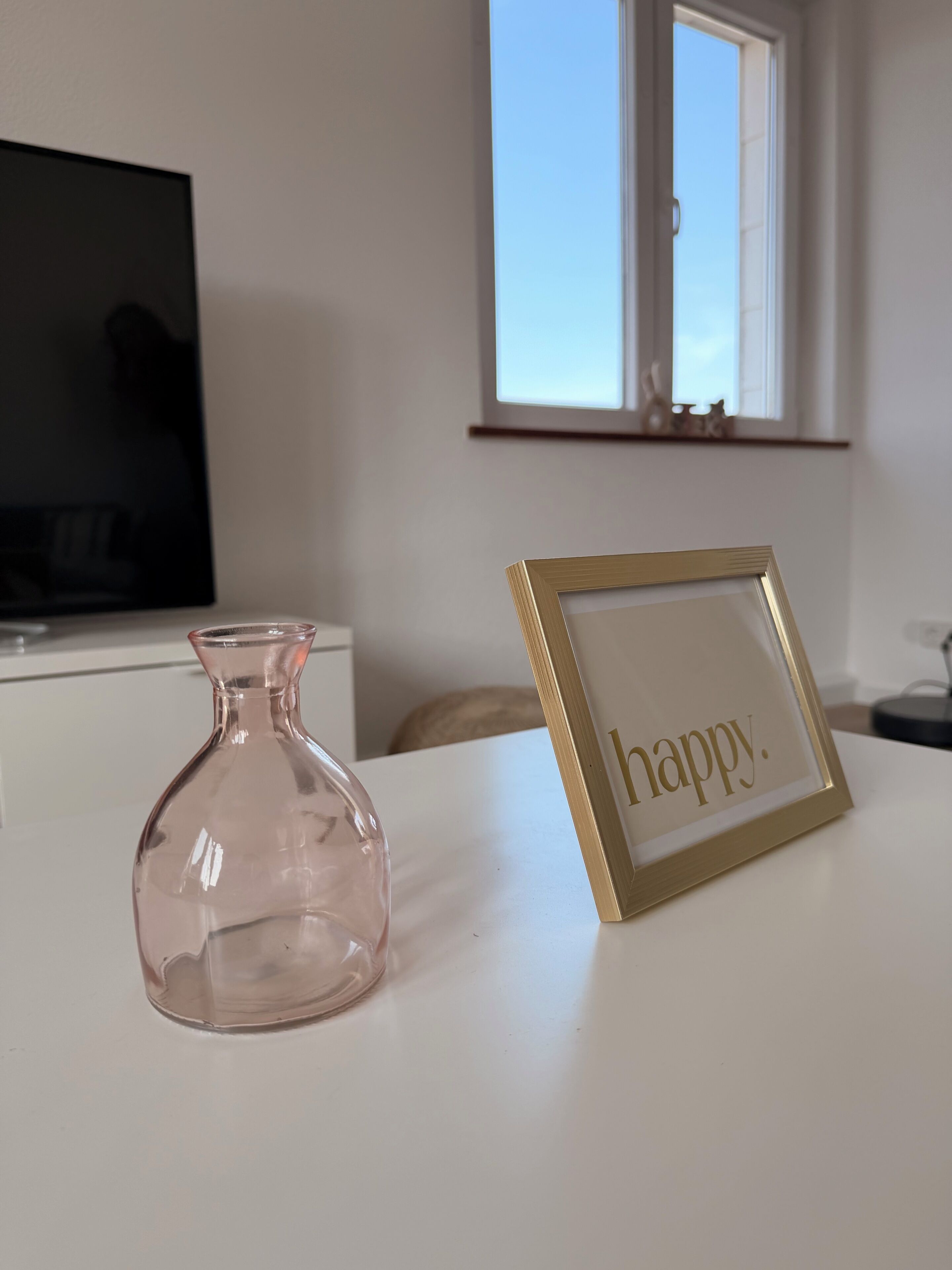 Ein Zimmer mit Fernseher, einer Vase und einem gerahmten Schild mit dem Wort 'happy'.