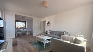 Una sala de estar moderna con un sofá gris, una mesa de centro blanca y un comedor con una mesa y sillas blancas.