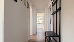 Un pasillo con piso de madera, un banco y ganchos en la pared.