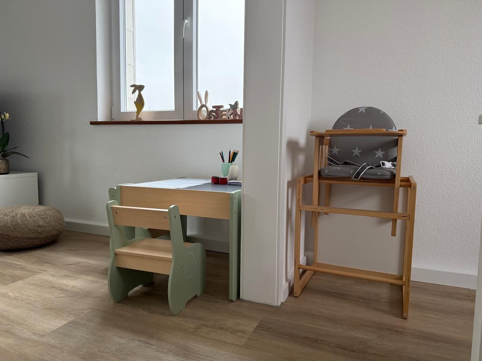 Una habitación con un escritorio de madera, una silla verde, un estante pequeño y una ventana.