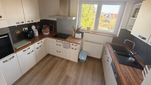 Una cocina moderna con armarios blancos, encimera negra, cocina integrada y ventana con vistas a árboles.