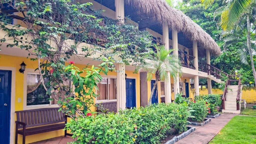 A two-story building with a thatched roof, balconies, and a garden area with various plants and flowers.