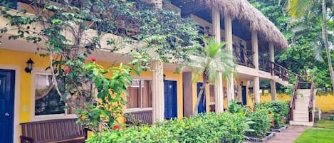 A two-story building with a thatched roof, balconies, and a garden area with various plants and flowers.