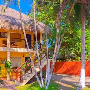 A yellow building with a thatched roof, a staircase, and palm trees. - Hotel Cafe Del Sol (Monterrico)