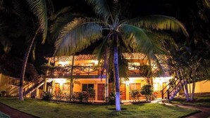 A two-story building with a balcony, surrounded by palm trees and a well-lit pathway. - Hotel Cafe Del Sol (Monterrico)
