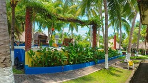 A tropical resort with palm trees, a thatched-roof building, and a pathway leading to a seating area. - Hotel Cafe Del Sol (Monterrico)