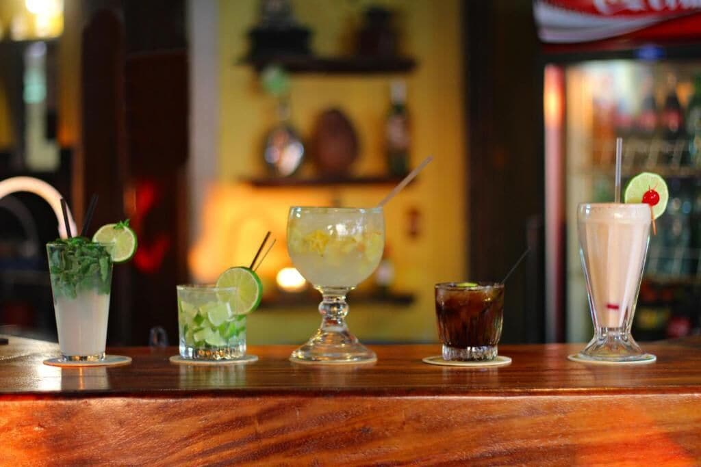 Un bar proposant une variété de boissons, notamment un mojito, une margarita, un cocktail décoré d’une tranche de citron vert, un soda foncé et un lait frappé à la cerise.