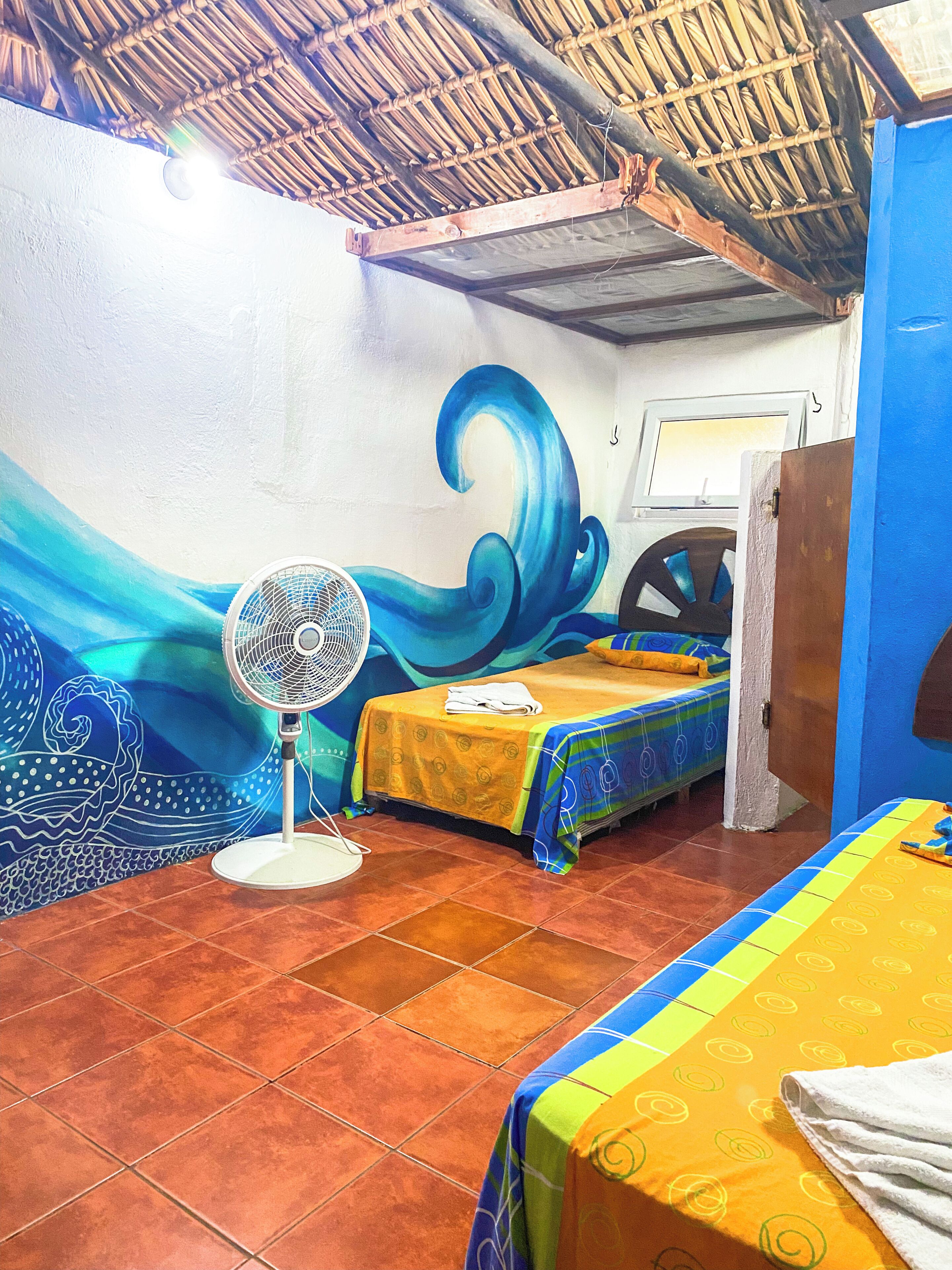 Una habitación con una cama, un ventilador y un mural.