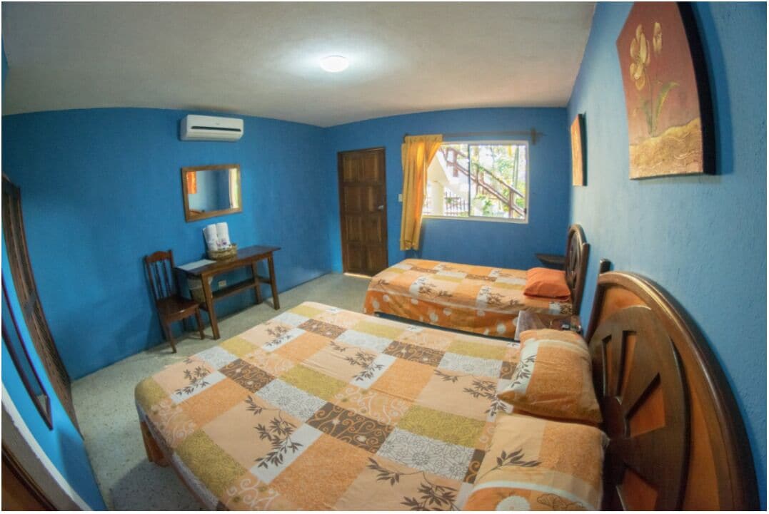 A bedroom with two beds, a desk, a chair, an air conditioner, and a window with curtains.