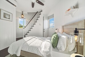 Ein Schlafzimmer mit Bett, Treppe, Fenster und Deckenventilator.