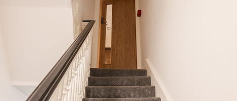 Uma escadaria com corrimão, degraus carpetados e uma porta no topo.