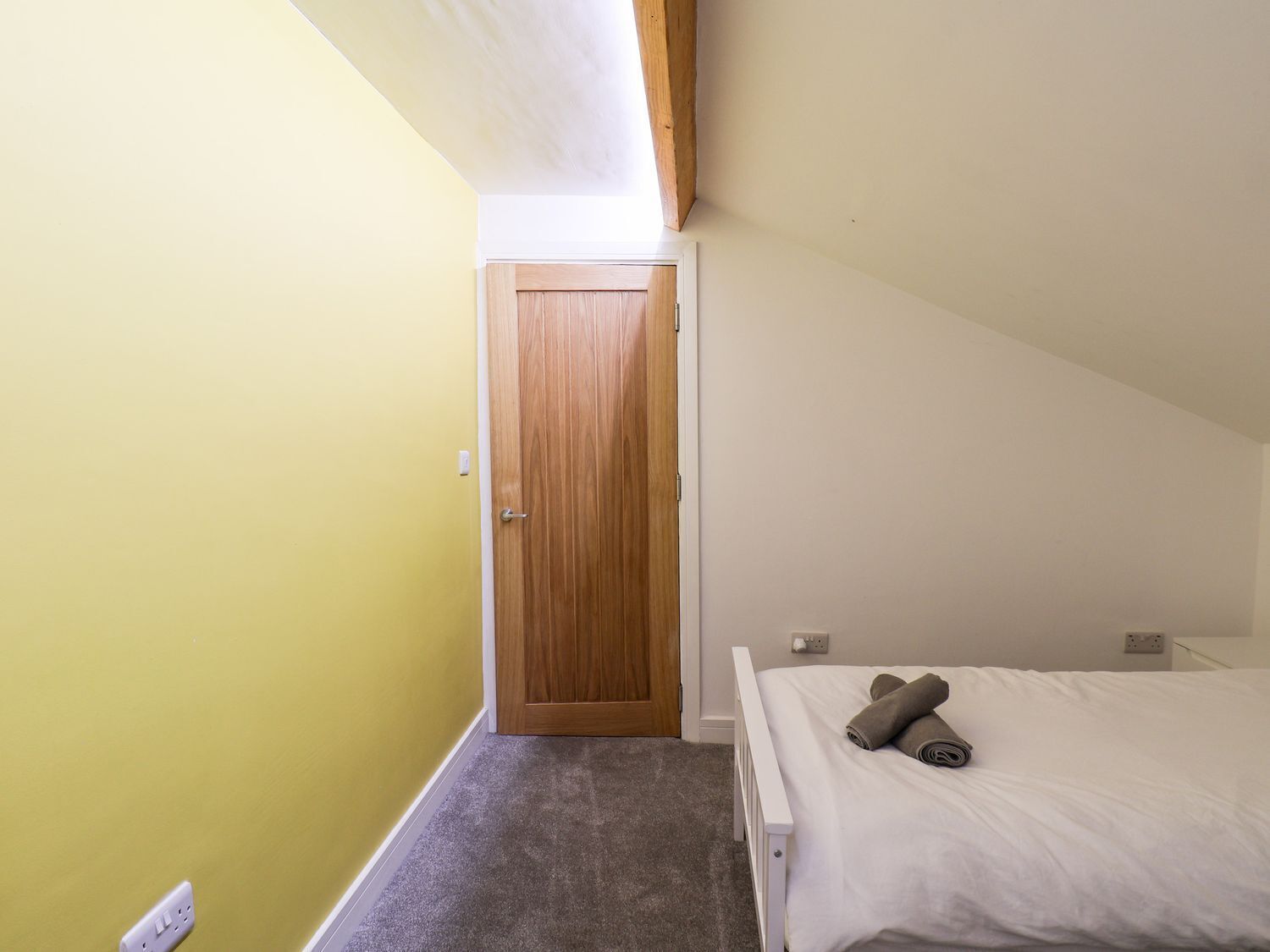 A bedroom with a single bed, a wooden door, and a small window.