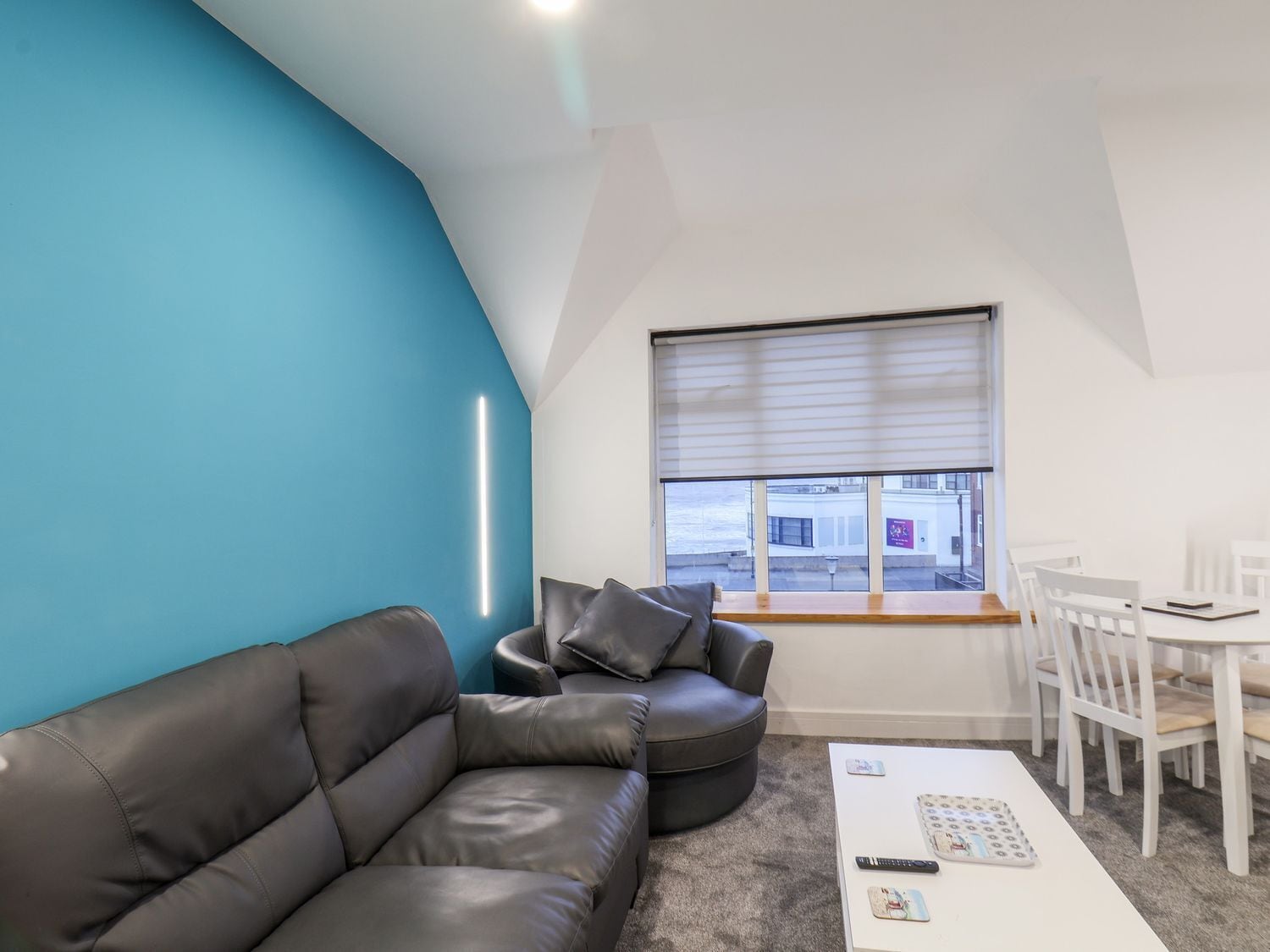 A modern living room with a blue accent wall, a leather sofa, a white coffee table, and a dining area with white chairs.