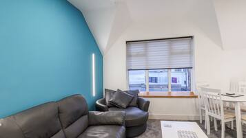 A modern living room with a blue accent wall, a leather sofa, a white coffee table, and a dining area with white chairs.