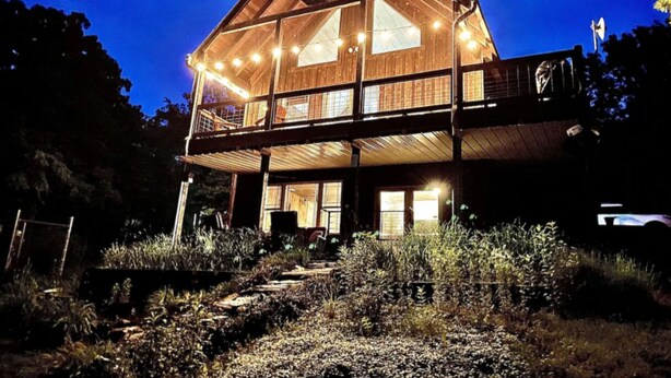 Eine große Holzhütte mit vielen Fenstern und einem Balkon, umgeben von dichtem Grün.