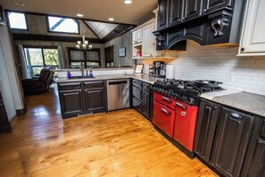A kitchen with dark cabinetry, a red stove, and a wooden floor. - Lake Front Retreat - Pool Table, Golf Cart, Kayaks (Lampe)