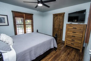 A bedroom with a bed, a wooden dresser, a television, and a ceiling fan. - Lake Front Retreat - Pool Table, Golf Cart, Kayaks (Lampe)