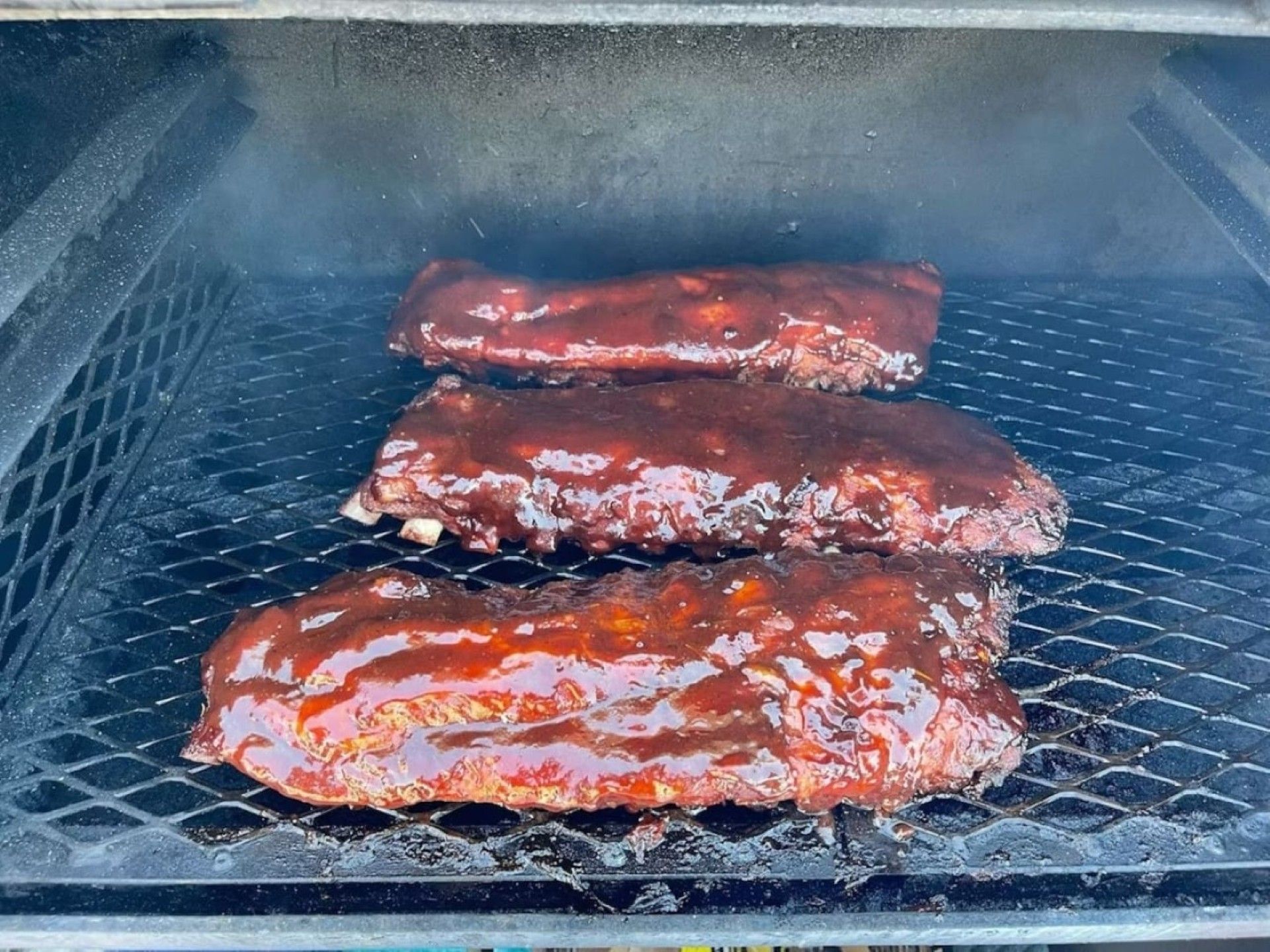 Three ribs cooking on a grill.