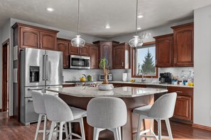 Une cuisine moderne dotée d’un grand îlot central, d’appareils électroménagers en acier inoxydable, de meubles en bois et de luminaires suspendus.