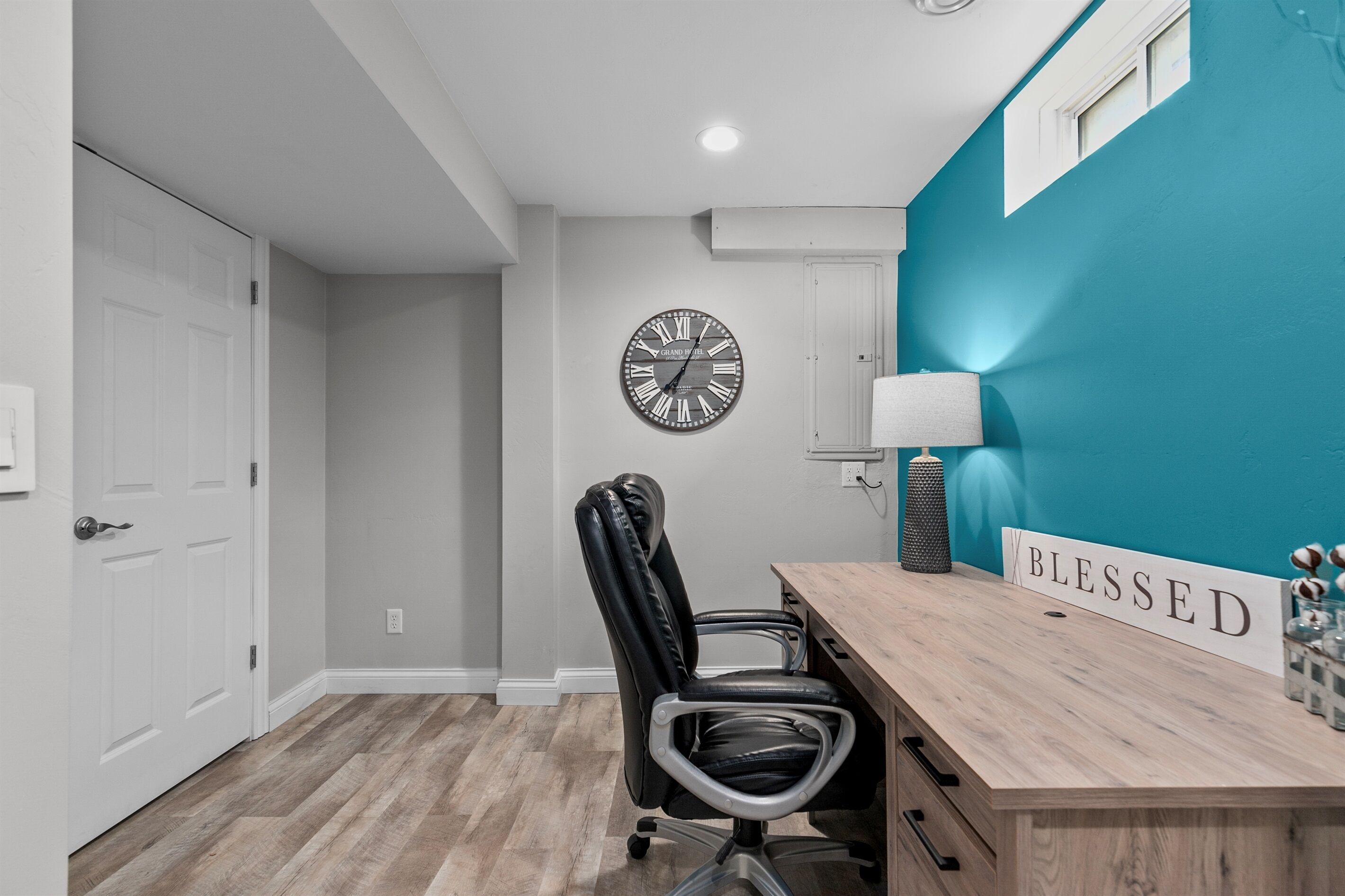 A room with a wooden desk, a black office chair, a clock on the wall, and a 'BLESSED' sign.