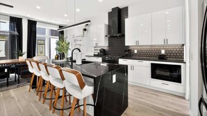 Una cocina moderna con armarios blancos, una isla con encimera negra y una zona de comedor con sillas blancas.