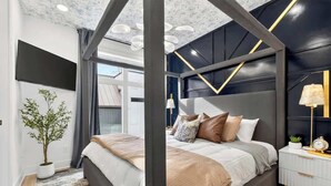 Un dormitorio moderno con cama, mesita de noche, lámpara y una planta en maceta.