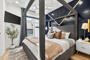 Ein modernes Schlafzimmer mit Bett, Nachttisch, Lampe und einer Topfpflanze.