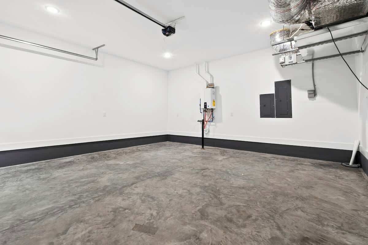 A spacious, empty room with a concrete floor, white walls, and a black baseboard.