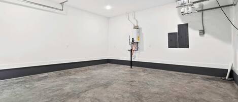 A spacious, empty room with a concrete floor, white walls, and a black baseboard.