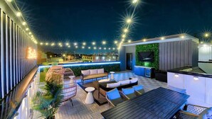 Un patio exterior con luces colgantes, un sofá, una mesa de comedor y una zona de cocina.