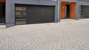 A modern two-story building with large windows, a garage, and a paved driveway. - Lux Home - 8 Beds | 3.5 Bath | Firepit Sleeps 12! (Nashville)